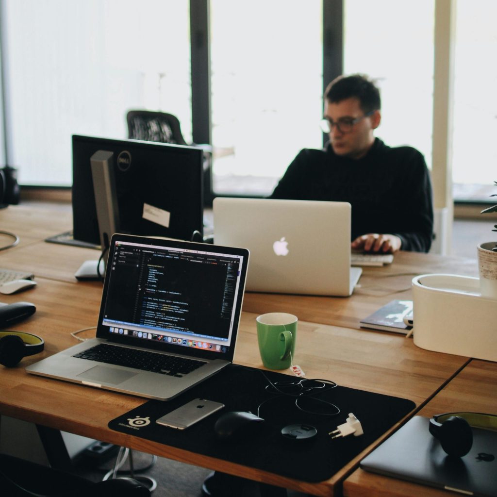 A web developer working on code in a modern office setting with multiple devices.